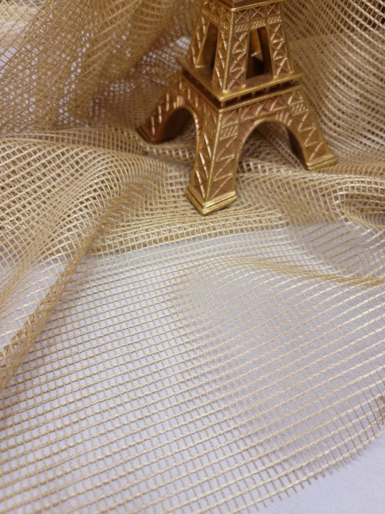 May include: A gold-colored Eiffel Tower replica figurine on a beige mesh fabric background.