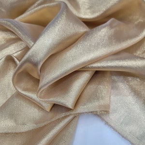 May include: A close-up of a piece of gold fabric with a subtle shimmer. The fabric is soft and flowing, with a slightly textured surface.