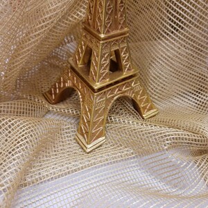May include: A gold-colored Eiffel Tower replica figurine on a brown burlap background.