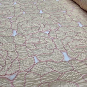 May include: A roll of fabric with a floral design. The fabric has a beige base with pink outlines, creating a textured, layered effect. The design features overlapping flower petals. The fabric is suitable for various craft projects.