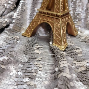 May include: A gold-colored Eiffel Tower replica figurine on a silver sequined fabric background.