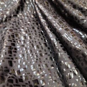 May include: Black fabric with a silver geometric pattern. The fabric has a shiny, metallic finish.