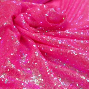 Puede incluir: Paillettes iridiscentes rosas sobre una tela de malla transparente. Las lentejuelas son pequeñas y redondas, y crean un efecto brillante.