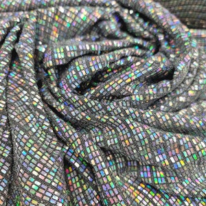 May include: Close-up of iridescent black fabric with a textured, shimmering pattern. The fabric is made of small, square sequins that reflect light in a variety of colours.