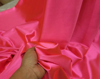 May include: A bright pink satin fabric with a smooth, silky texture. The fabric is draped and folded, showcasing its luxurious feel.