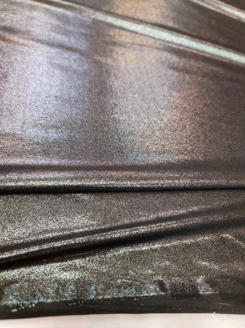 May include: Close-up of a metallic fabric with a subtle iridescent sheen. The fabric has a textured surface and is folded in a few places.