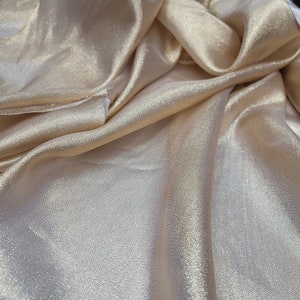 May include: A close-up of a gold satin fabric with a subtle shimmer. The fabric is draped and folded, showcasing its soft texture.