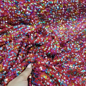 May include: Close-up of red fabric covered in iridescent sequins. The sequins are small and round, reflecting a rainbow of colors. The fabric is slightly ruffled, creating texture and depth. This material is suitable for apparel and craft projects.