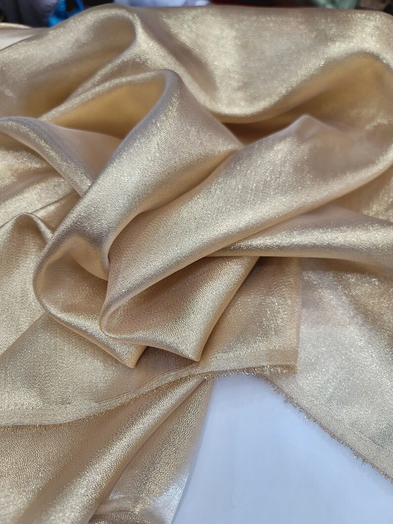 May include: A close-up of a piece of gold fabric with a subtle shimmer. The fabric is folded and draped, showcasing its soft texture.