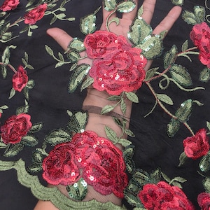 May include: A sheer black mesh fabric featuring an intricate floral embroidery pattern. The design consists of vibrant red roses with detailed green leaves and stems, accented with small, shimmering sequins throughout the floral motifs.