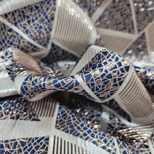 May include: Close-up of a white fabric with a geometric pattern of blue and gold triangles. The fabric has a textured, woven look.