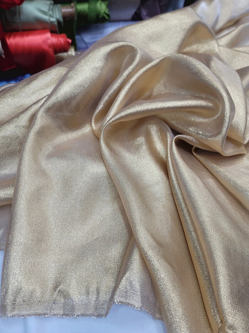May include: A close-up of a gold satin fabric with a subtle shimmer. The fabric is folded and draped, showcasing its soft texture.