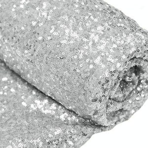 May include: Silver sequin fabric with a shiny, sparkly finish. The fabric is rolled up and the sequins are visible on both sides.