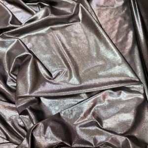 May include: Close-up of a metallic fabric with a shimmering, iridescent finish. The fabric is draped and folded, creating a textured and luxurious look.