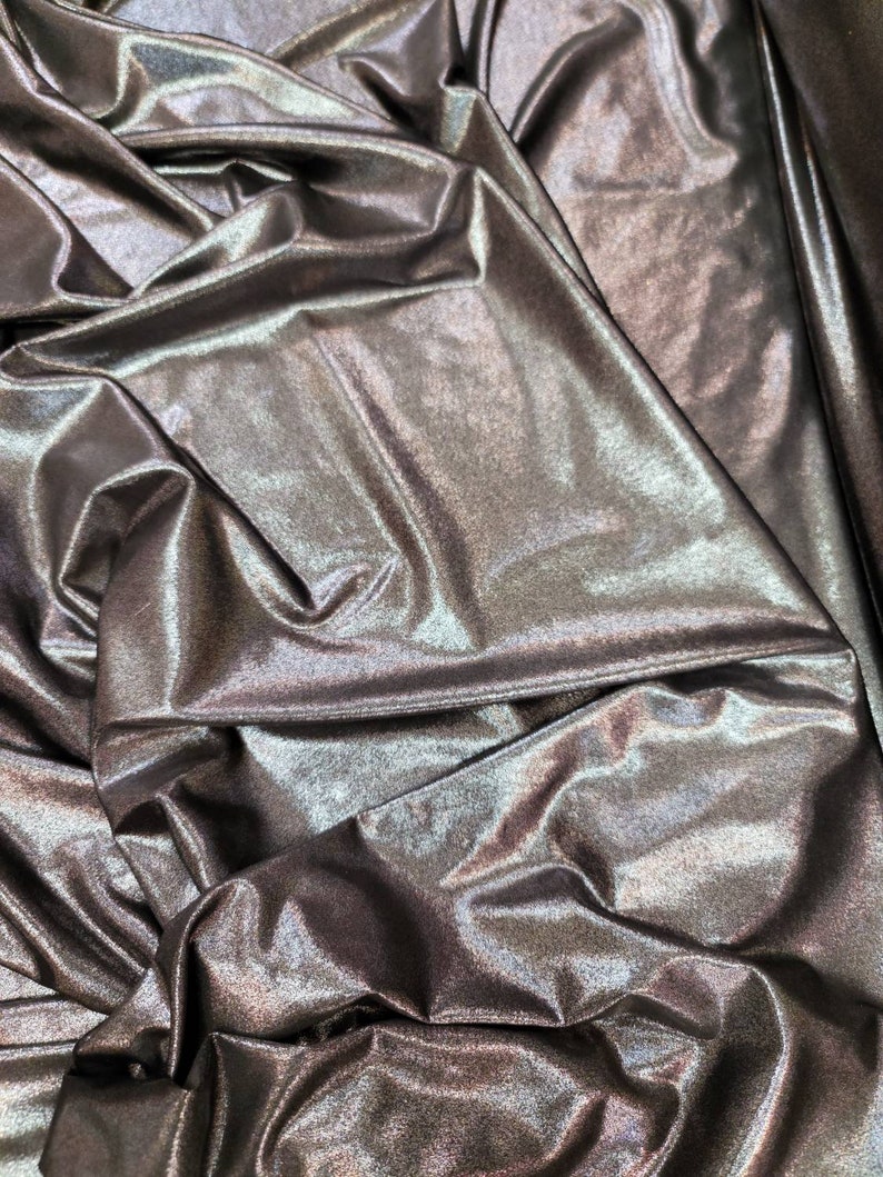 May include: Close-up of a metallic fabric with a shimmering, iridescent finish. The fabric is draped and folded, creating a textured and luxurious look.