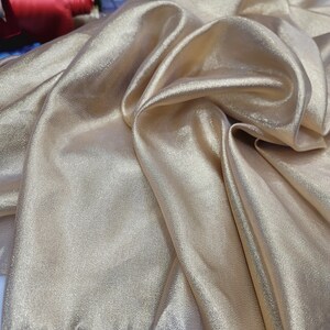 May include: A close-up of a gold fabric with a subtle shimmer. The fabric is folded and draped, showcasing its soft texture.