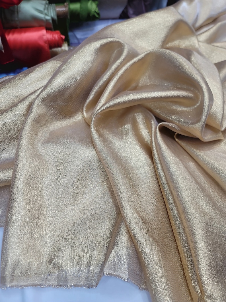 May include: A close-up of a gold fabric with a subtle shimmer. The fabric is folded and draped, showcasing its soft texture.