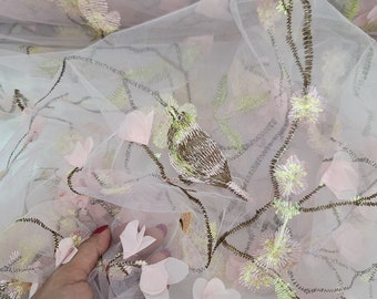May include: Pink tulle fabric with embroidered floral designs in pink, green, and brown. The fabric has a delicate, airy feel and is perfect for creating garments, accessories, or home decor.