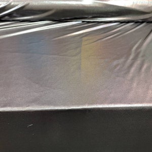 May include: A close-up of iridescent black fabric with a subtle rainbow sheen. The fabric is smooth and has a slight sheen.