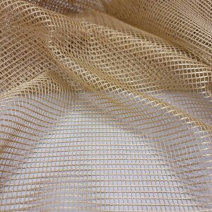 May include: A close-up of a beige mesh fabric with a square grid pattern. The fabric is soft and has a subtle sheen.