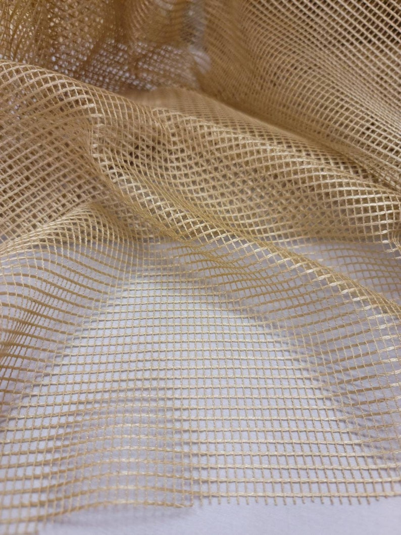 May include: A close-up of a beige mesh fabric with a square grid pattern. The fabric is soft and has a subtle sheen.