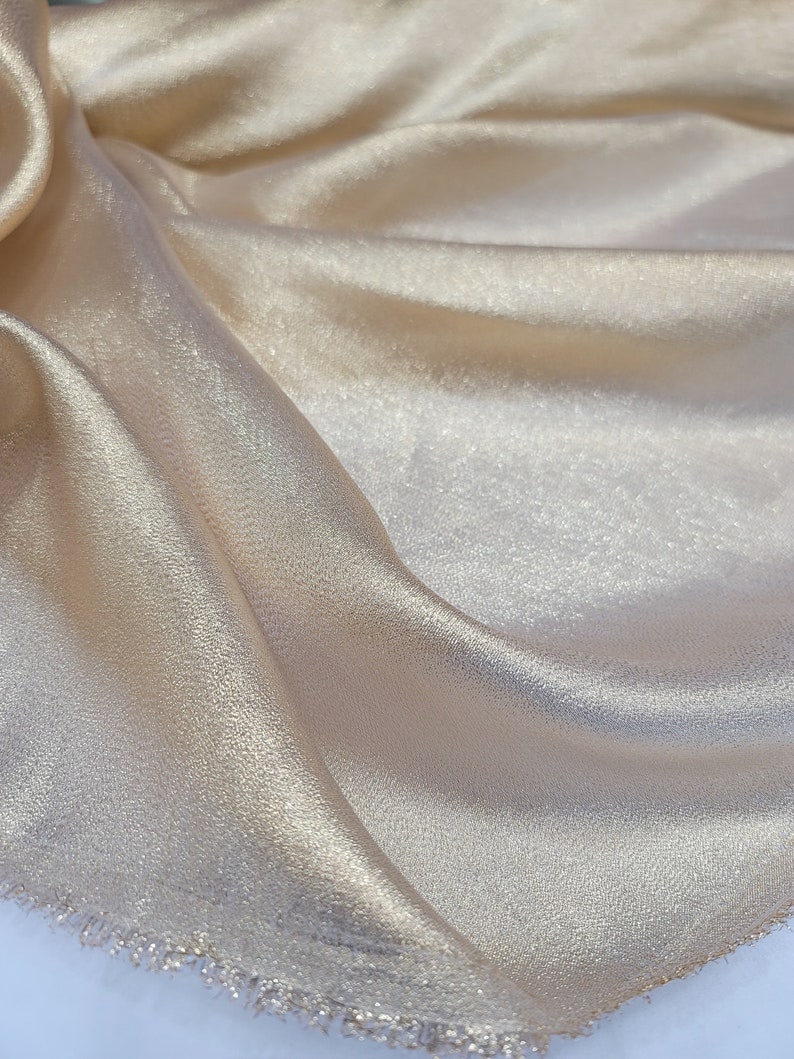 May include: A close-up of a piece of gold fabric with a subtle shimmer. The fabric has a slightly textured surface and a fringed edge.