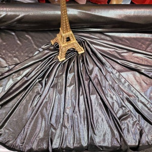 May include: A close-up of iridescent black fabric with a gold Eiffel Tower figurine on top. The fabric is draped and folded, creating a soft, flowing look.