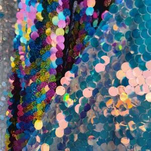 May include: Close-up of iridescent blue, pink, and green sequins on a fabric. The sequins are arranged in a random pattern and are very shiny.