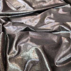 May include: Close-up of a silver metallic fabric with a subtle shimmer. The fabric is wrinkled and folded, creating a textured surface.