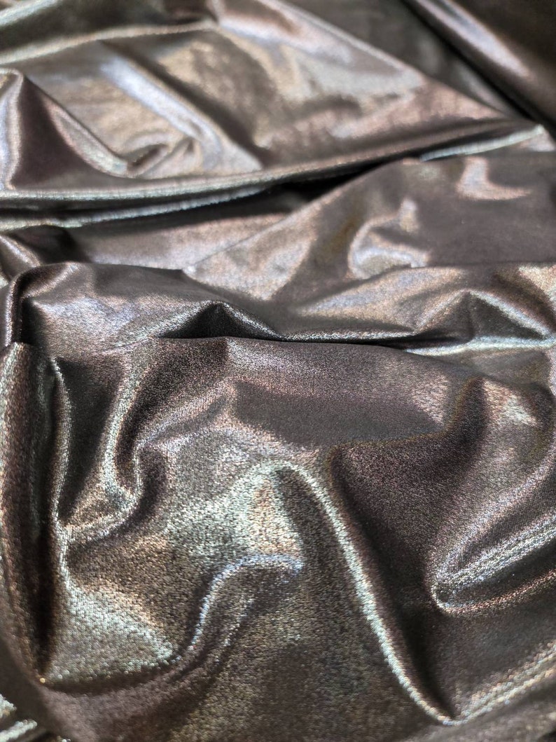 May include: Close-up of a silver metallic fabric with a subtle shimmer. The fabric is wrinkled and folded, creating a textured surface.