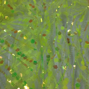 Op de afbeelding: Groen doorschijnend stof met groene en gouden pailletten in de vorm van een klavertje vier.