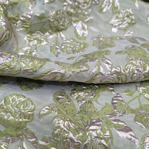 May include: Green and silver floral fabric with a textured, embossed design. The fabric has a sheer, translucent quality.