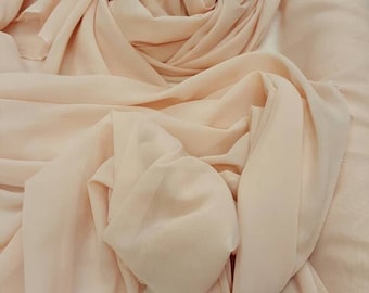 Könnte beinhalten: Ein peachfarbener, durchsichtiger Stoff, der über eine weiße Oberfläche gelegt wird. Eine einzelne rote Rose mit grünen Blättern liegt auf dem Stoff.