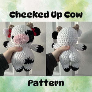 Puede incluir: Un patrón de crochet para una vaca blanca y negra con lazos rojos. El patrón se llama "Cheeked Up Cow".