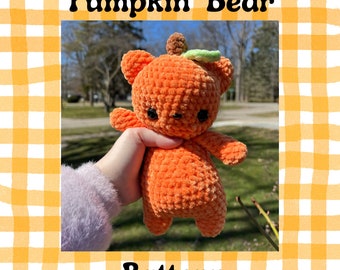 May include: A crocheted pumpkin-shaped bear with a green leaf on its head. The bear is orange and has black eyes. The bear is being held by a hand.