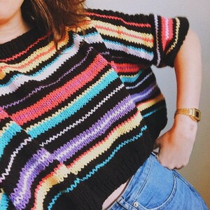 Puede incluir: Un suéter de rayas blancas y negras con rayas de colores en rosa, amarillo, azul y morado. El suéter está tejido y tiene un corte holgado.