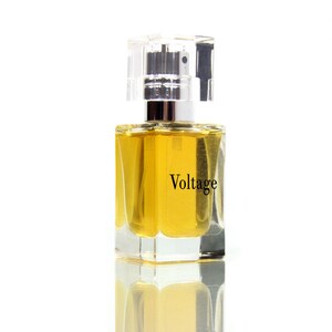 May include: A clear glass bottle of perfume with a silver cap. The bottle is filled with a yellow liquid and the label reads "Voltage".