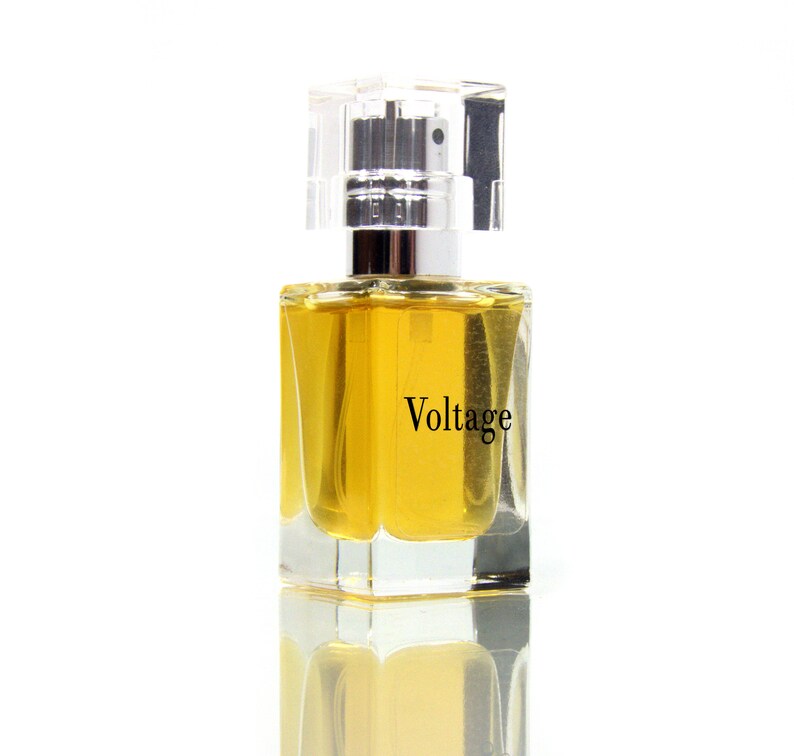May include: A clear glass bottle of perfume with a silver cap. The bottle is filled with a yellow liquid and the label reads "Voltage".