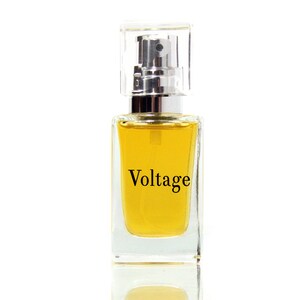 May include: A clear glass bottle of perfume with a silver spray nozzle and a yellow liquid. The bottle has a black label with the word "Voltage" printed on it.