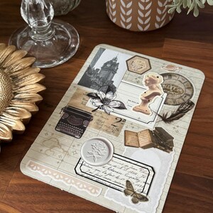 Peut inclure: Un collage de style vintage avec une image en noir et blanc d'un bâtiment, une machine à écrire, un livre, une plume, un sceau de cire, un papillon et une note manuscrite. Le collage est sur un fond crème avec une bordure en dentelle blanche.