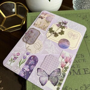 May include: A purple and white scrapbook page with various decorative stickers featuring flowers, butterflies, and a grid pattern. The stickers are arranged in a collage style.