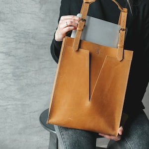 A smiling woman is holding a yellow leather tote bag. She pulls out the laptop out of it.