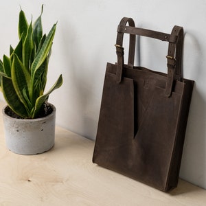 A brown leather tote sitting on the table next to the plant.