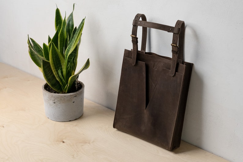 A brown leather tote sitting on the table next to the plant.