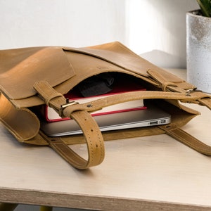 A yellow leather tote is sitting on top of the wooden table. Inside the tote bag are laptop and a book.