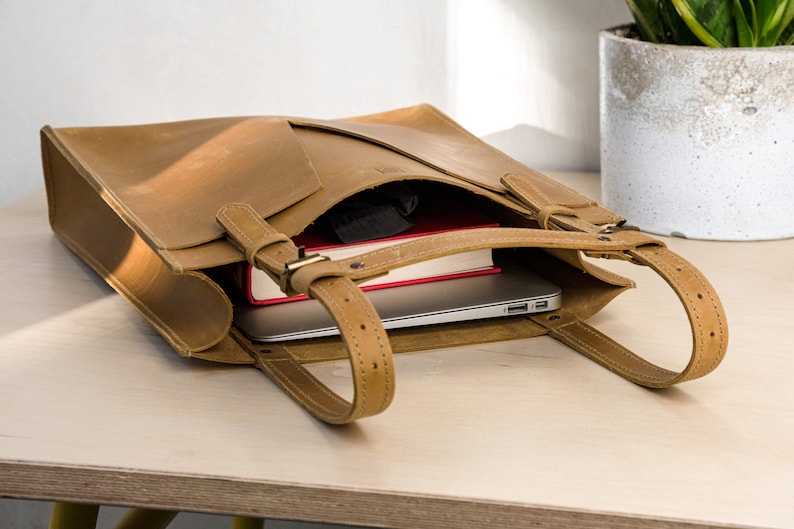 A yellow leather tote is sitting on top of the wooden table. Inside the tote bag are laptop and a book.