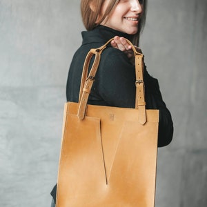 A woman is holding a yellow leather tote on her right shoulder.