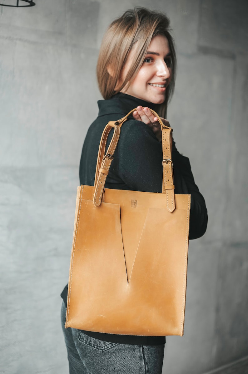 A woman is holding a yellow leather tote on her right shoulder.
