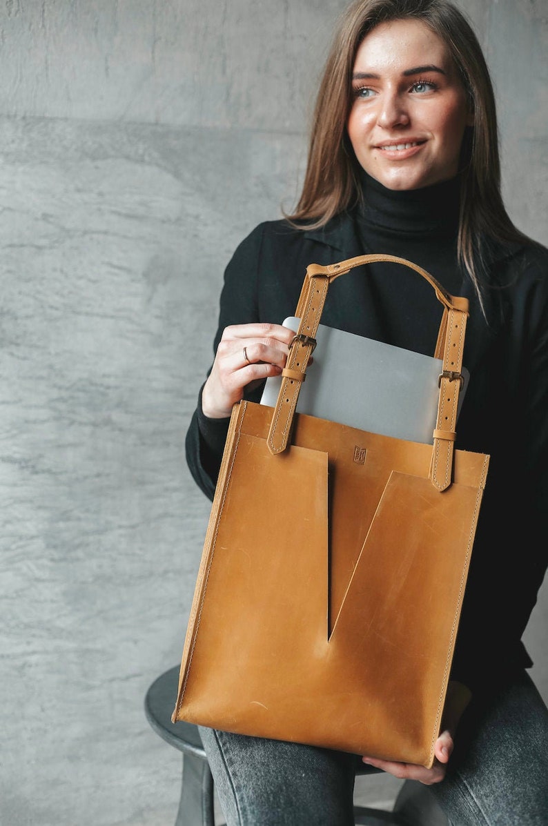 A smiling woman is holding a yellow leather tote bag. She pulls out the laptop out of it.