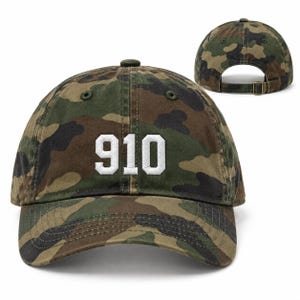 May include: A camouflage baseball cap featuring the number 910 embroidered in white on the front panel. The cap has a curved brim, stitched eyelets, and an adjustable strap with a metal buckle at the back for a secure fit and classic style.
